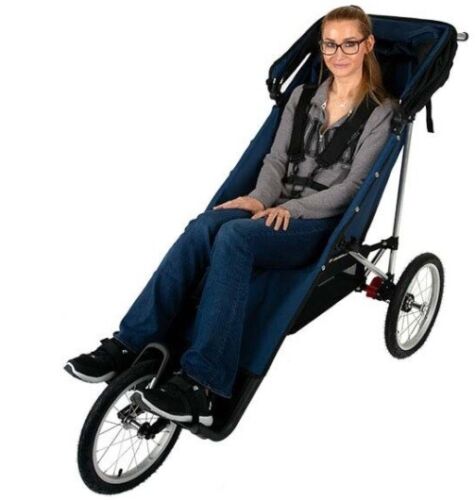 Image of a person with long hair and glasses sitting in a larger three-wheeled  push chair. 
